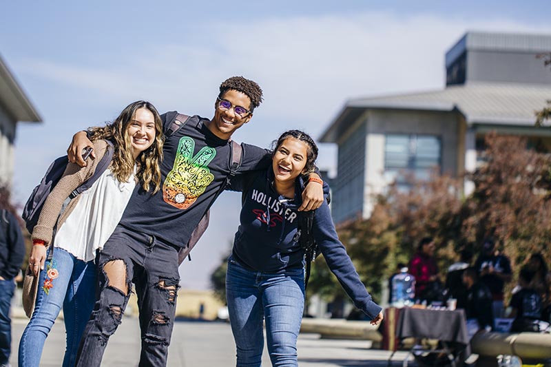 three students with one arm over each others necks smiling